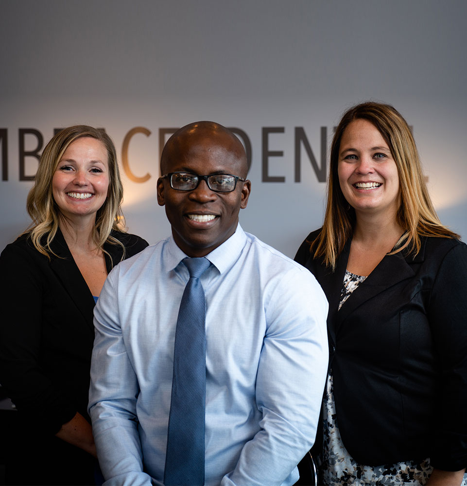 Embrace Dental Care Dr Rinto Adeniran and Staff Posing In Front Of Wall Logo