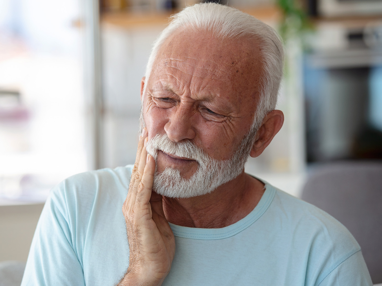 Older man holding his jaw in pain from a dental emergency, in need of a 24-hour emergency dentist in Louisville